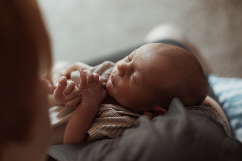 Motherhood Photographer, A newborn baby sleeps snuggled into blankets